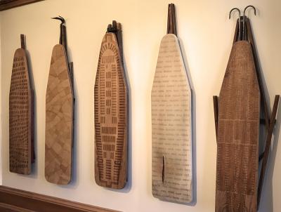 photo of 5 antique wooden ironing boards with patterns and words burned into them. They are the work of artist Marianetta Porter