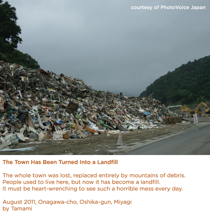 photo with text: The Town Has Been Turned Into a Landfill The whole town was lost, replaced entirely by mountains of debris. People used to live here, but now it has become a landfill. It must be heart-wrenching to see such a horrible mess every day. August 2011, Onagawa-cho, Oshika-gun, Miyagi by Tamami