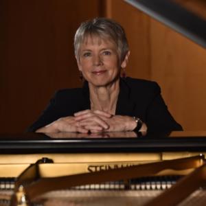 color photo of Ellen Rowe standing behind a grand piano