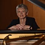 color photo of Ellen Rowe standing behind a grand piano