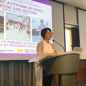 photo of Prof. Wang Zheng at a lectern. the screen behind her shows pictures of Chinese feminist activists