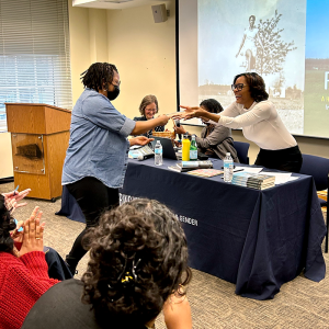 photo of Ava Purkiss handing a book to a woman across a table