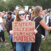 young woman at a protest holding a hand-written poster that reads "Intersectional Feminism Matters"