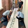 photo of three people working on the large scroll in Lane Hall's back hallway